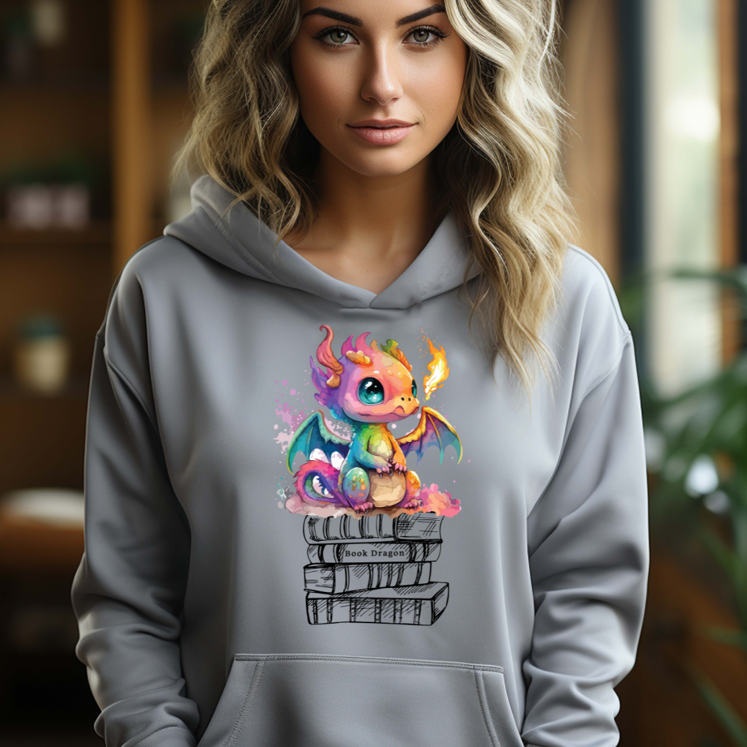 Young woman with long blonde hair wearing a grey book dragon hoodie with a fire breathing rainbow dragon sitting on top of a stack of books designed by graphic apparel shop Midnight Gypsy Designs as part of their bookish merch collection. Perfect book dragon shirt for fantasy readers!