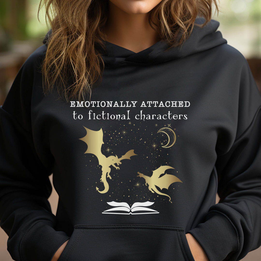 Young woman with shoulder length hair wearing a black Emotionally Attached to Fictional Characters hoodie with two gold dragons flying over an open book and a crescent moon created by graphic apparel company Midnight Gypsy Designs for their academia book merch collection. Perfect book dragon shirt, fantasy readers shirt, bookish merch, shirt for fantasy readers, and fourth wing hoodie!