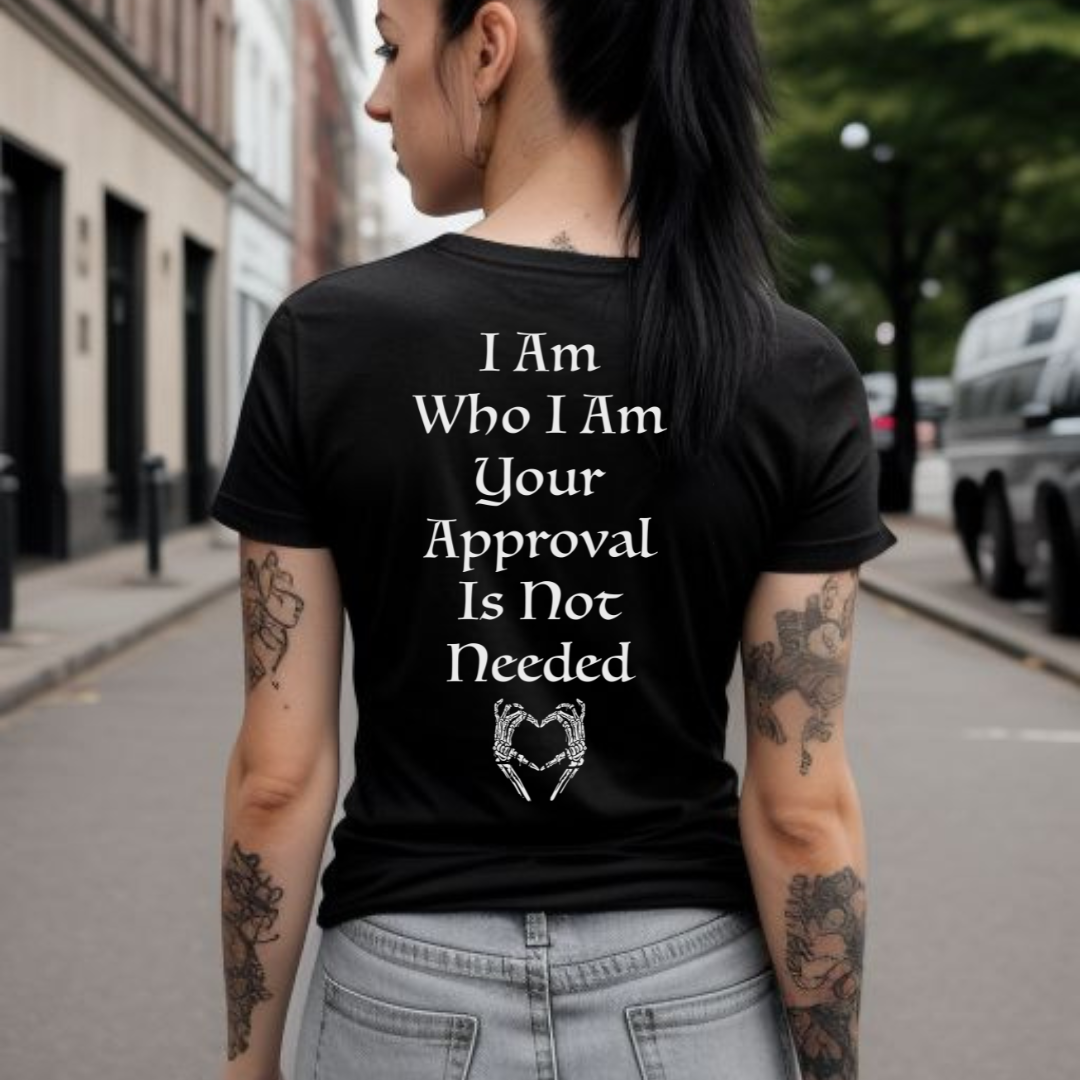 Young woman standing in city with black hair in a pony tail with tattoos wearing a black motivational shirt that says I am who I am your approval is not needed with skeleton hands giving the I heart you symbol created by graphic apparel company Midnight Gypsy Designs.
