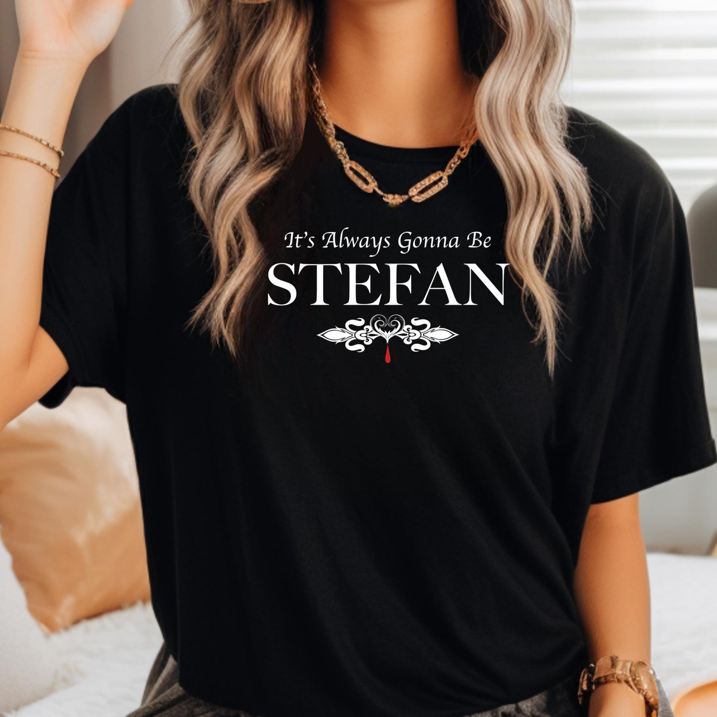 Young woman with long blonde hair wearing a necklace and a black t-shirt that reads It's Always Gonna Be Stefan from The Vampire Diaries created by apparel shop Midnight Gypsy Designs.