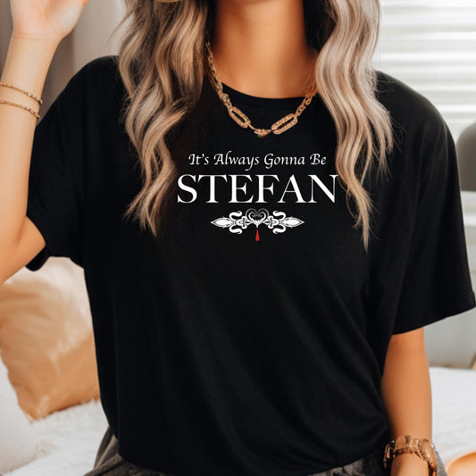 Young woman with long blonde hair wearing a necklace and a black t-shirt that reads It's Always Gonna Be Stefan from The Vampire Diaries created by apparel shop Midnight Gypsy Designs.