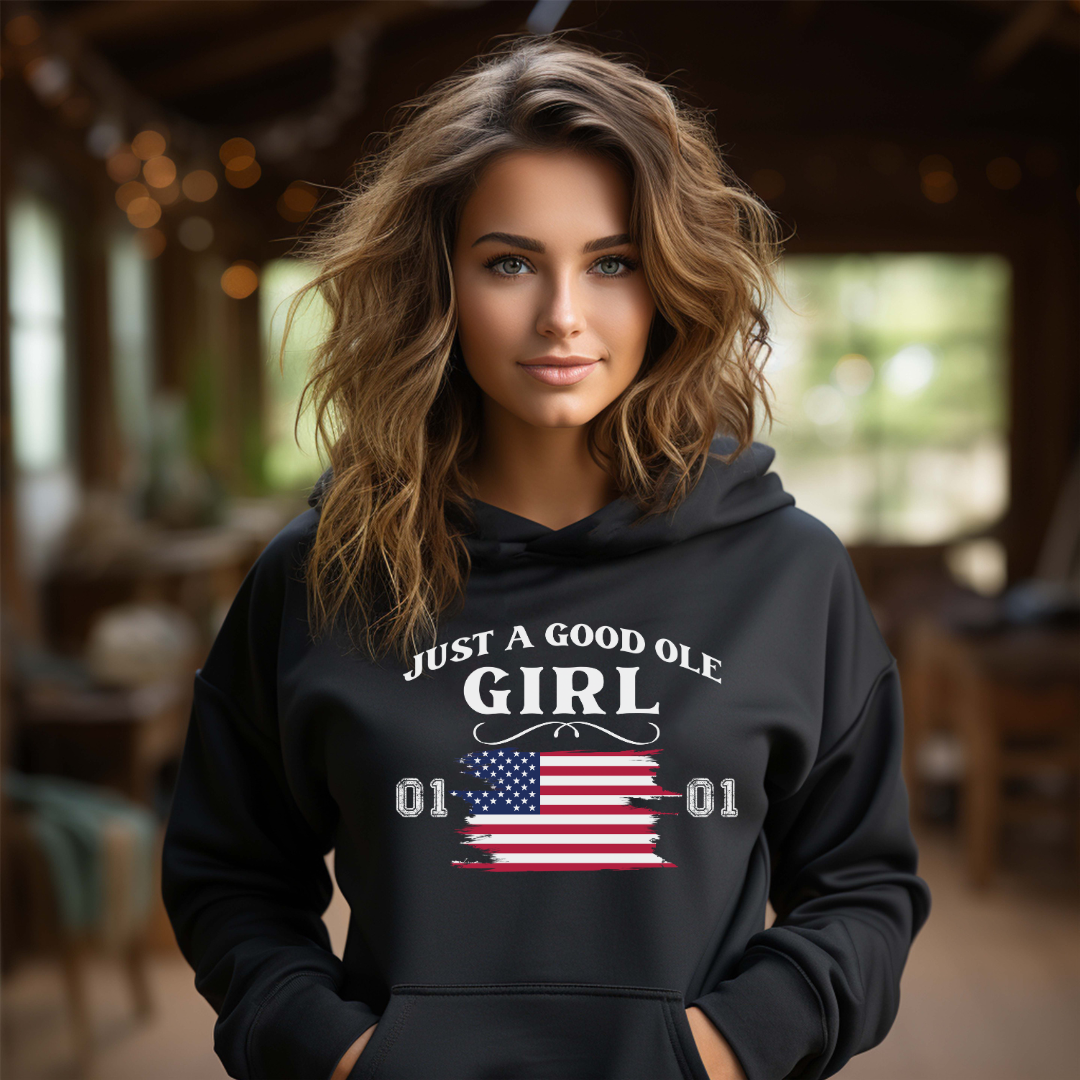 Young woman with wavy brown hair standing inside vintage southern room wearing a black Just A Good Ole Girl hoodie with American flag and General Lee 01 number created by graphic apparel company Midnight Gypsy Designs as part of their Patriotic Pride Apparel Collection. Perfect Dukes of Hazard hoodie, Dukes of Hazard shirt, Daisy Duke hoodie, Daisy Duke shirt, General Lee hoodie, General Lee shirt, and USA Patriotic shirt.
