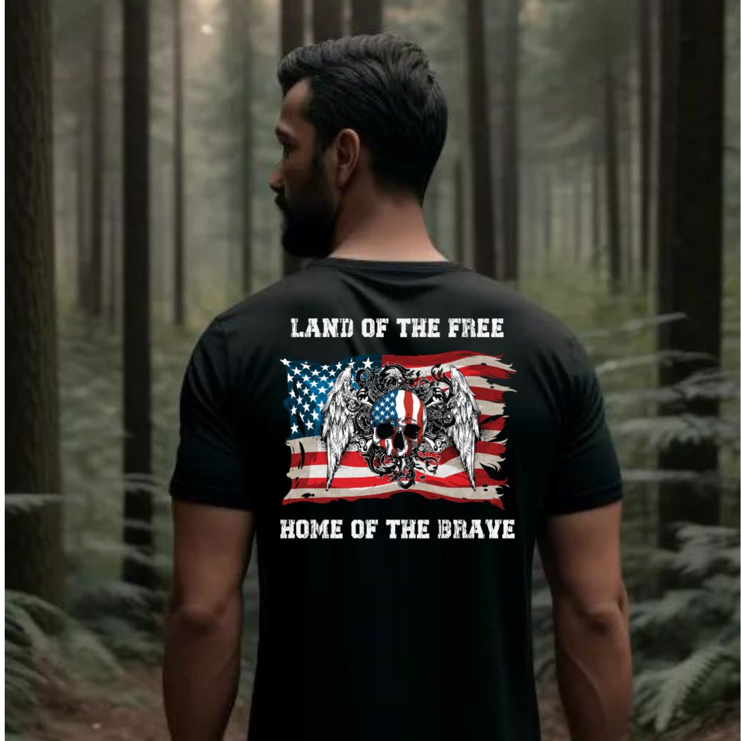 Man in woods with dark hair and a beard wearing a black patriotic t-shirt that reads Land of the Free Home of the Brave with the American flag and a skull with angel wings created by graphic apparel shop Midnight Gypsy Designs.