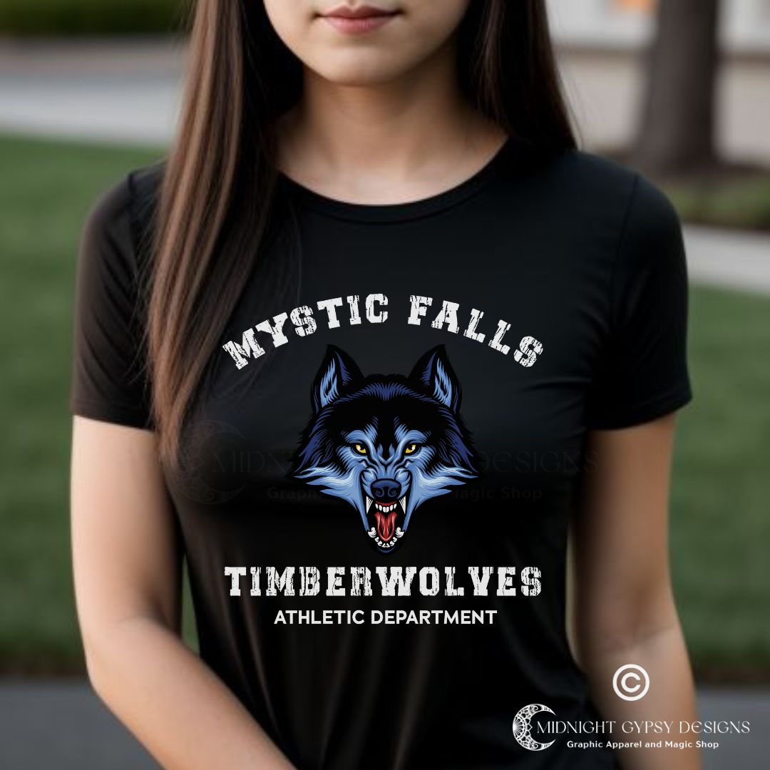 Young woman with long brown hair standing in Mystic Falls wearing a black Mystic Falls Timberwolves shirt with a blue werewolf showing its fangs created by graphic apparel company Midnight Gypsy Designs as part their The Vampire Diaries merch collection. Perfect The Vampire Diaries shirt, Mystic Falls shirt, Mystic Falls Timberwolves t-shirt, Stefan Salvatore shirt, Stefan Salvatore t-shirt, Stefan Salvatore tee, Stefan Salvatore 17 shirt, Mystic Falls High School shirt, Team Stefan shirt, Team Damon Shirt.