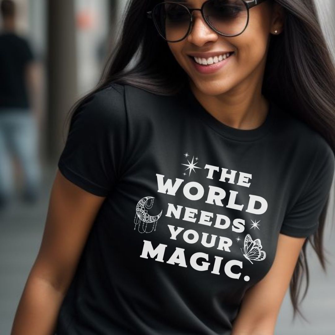 Woman in sunglasses wearing a The World Needs Your Magic T-shirt as a mental health awareness shirt. Black kindness shirt with white lettering, stars, moon, and butterfly.