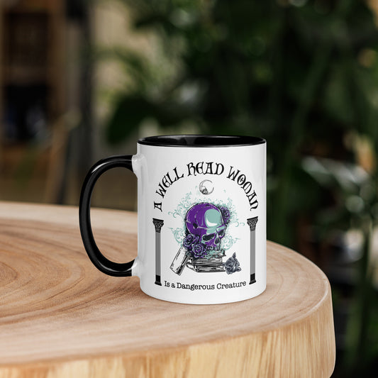 Black and white ceramic coffee mug with words A Well Read Woman Is a Dangerous Creature with a purple skull with roses on top of a stack of books from bookish shop Midnight Gypsy Designs.