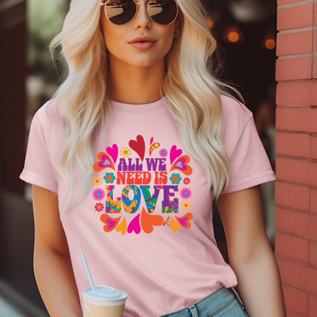 Young woman with blonde hair and sunglasses holding a coffee cup wearing an All We Need Is Love T-shirt by Midnight Gypsy Designs apparel company.