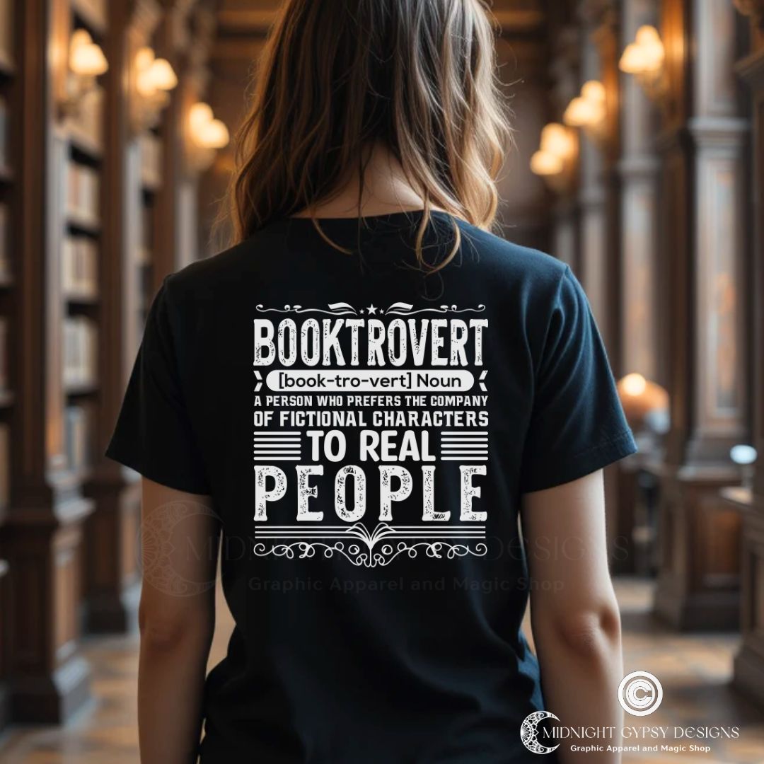 Young woman wearing a black booktrovert definition t-shirt with 'Booktrovert' definition in bold white letters in a library setting created by graphic apparel company Midnight Gypsy Designs as part of their bookish merch clothing line.