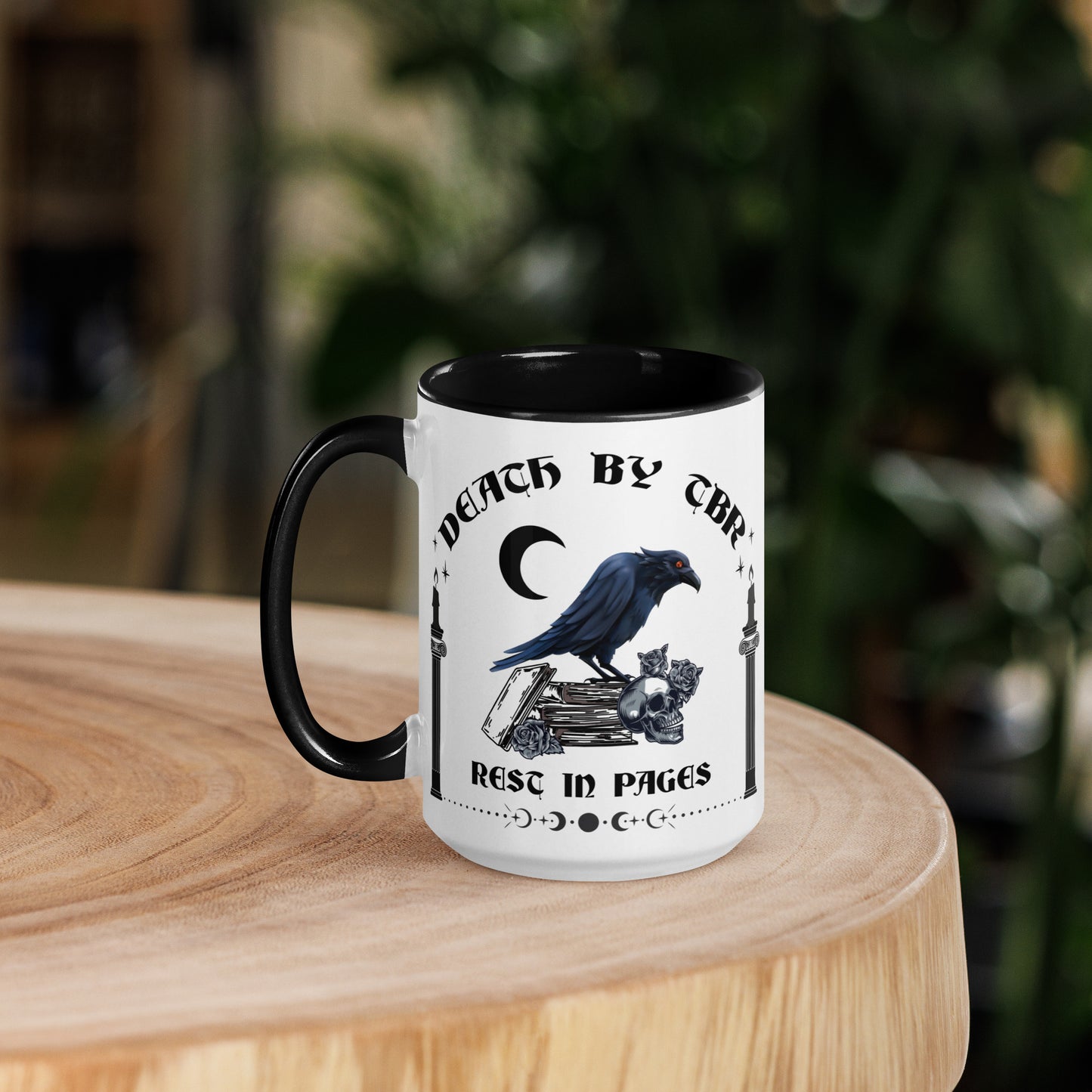 Black and white ceramic mug that reads Death By TBR Rest In Pages with moon, raven standing on a book stack, a skull, and two burning candles from bookish shop Midnight Gypsy Designs.