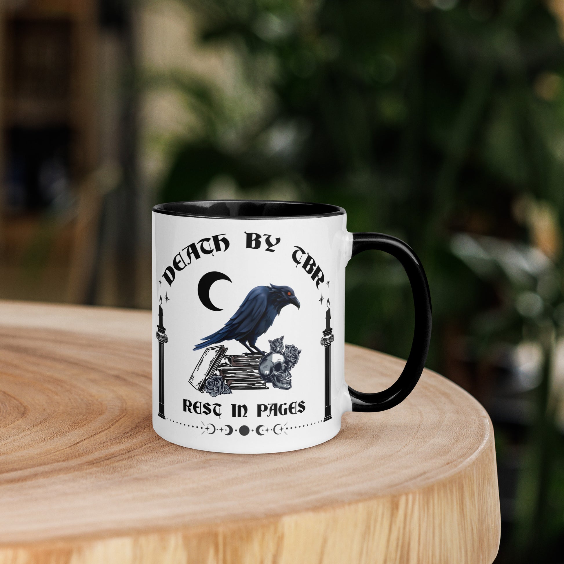 Black and white ceramic mug that reads Death By TBR Rest In Pages with moon, raven standing on a book stack, a skull, and two burning candles from bookish shop Midnight Gypsy Designs.