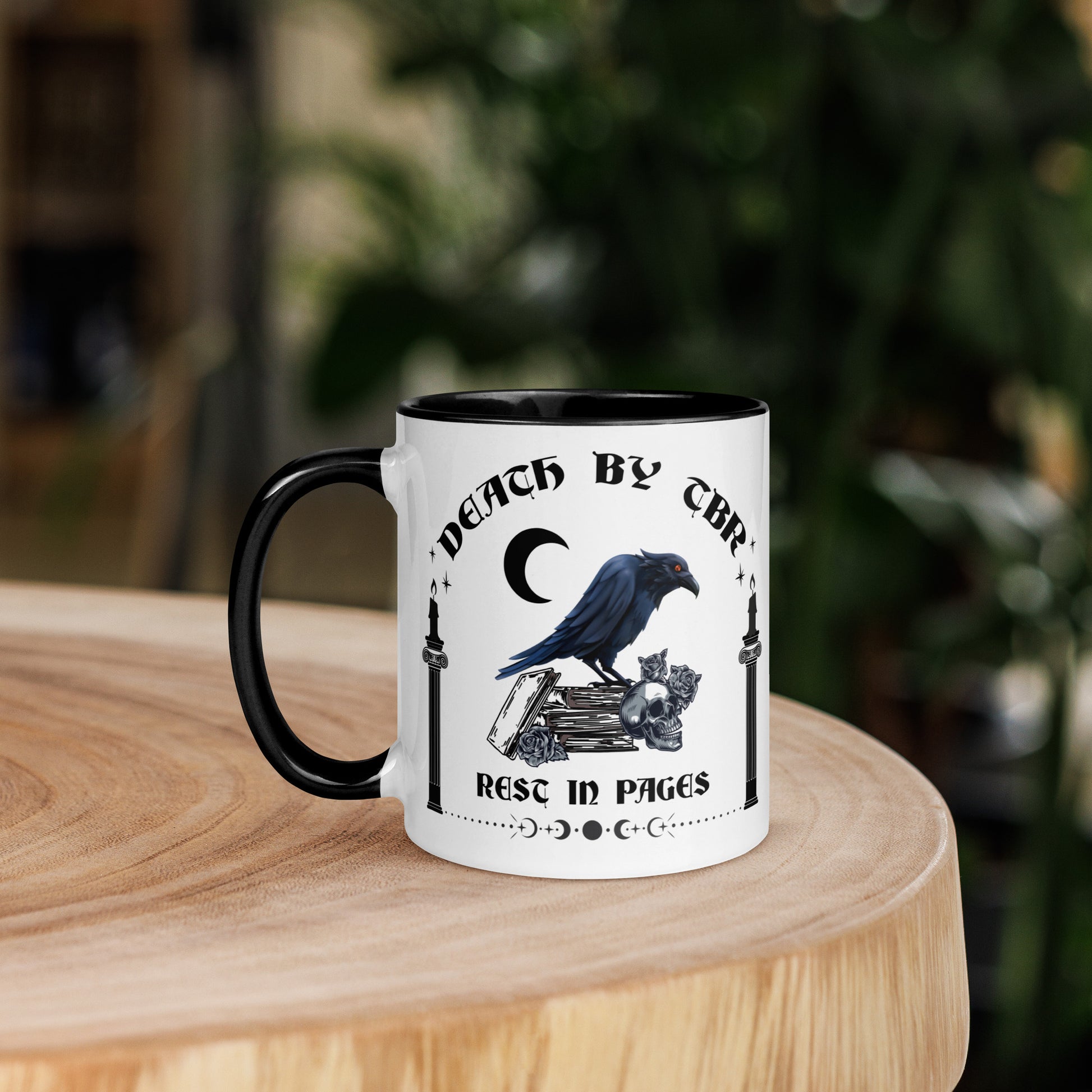 Black and white ceramic mug that reads Death By TBR Rest In Pages with moon, raven standing on a book stack, a skull, and two burning candles from bookish shop Midnight Gypsy Designs.