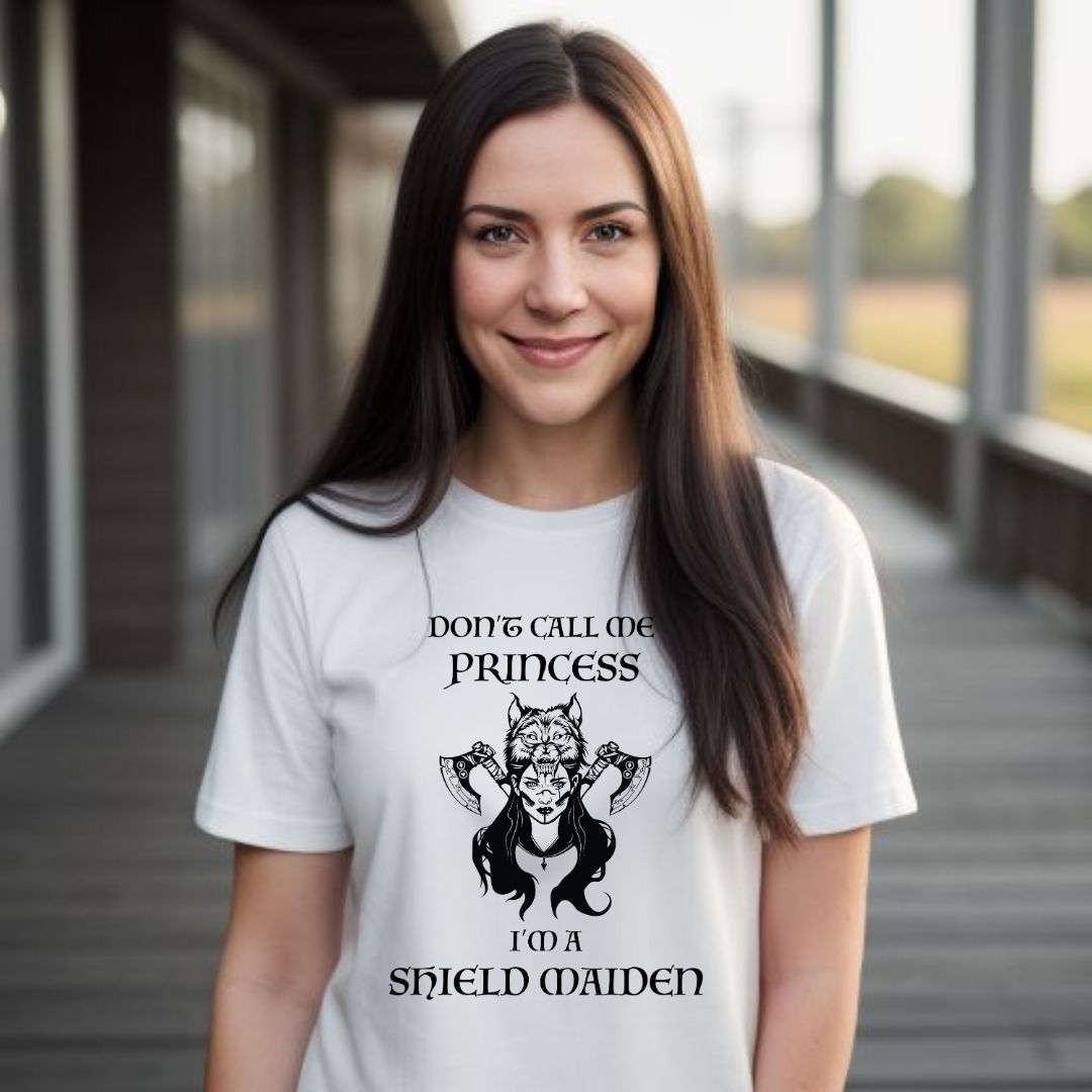 Young woman with long brown hair smiling while wearing a white t-shirt with lettering that says Don't Call Me Princess I'm a Shield Maiden with a female Viking Warrior with Norse Viking axes and a wolf created by apparel shop Midnight Gypsy Designs.