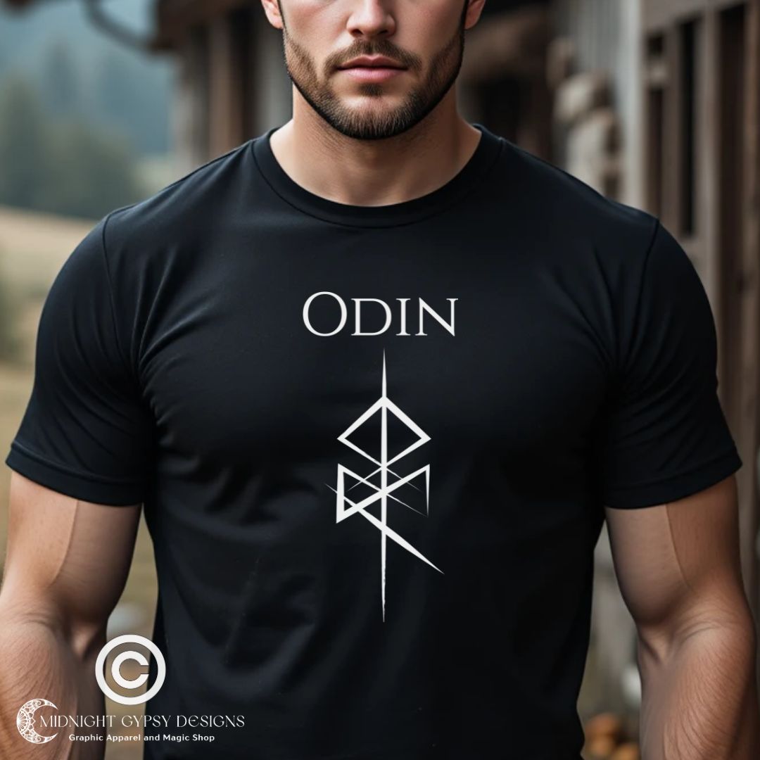 Young man with muscles and near shaven beard standing outside in Norway wearing a black viking t-shirt that reads Odin with the Odin God of War Futhark rune symbol created by Norse Viking apparel shop Midnight Gypsy Designs as part of their Viking apparel clothing line. Perfect Odin God of War t-shirt.