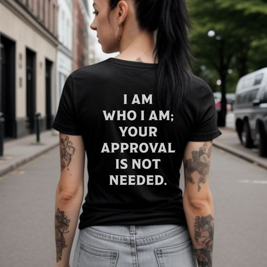 Young woman standing in city with black hair in a pony tail with tattoos wearing a black slogan shirt that says I am who I am your approval is not needed created by apparel company Midnight Gypsy Designs.