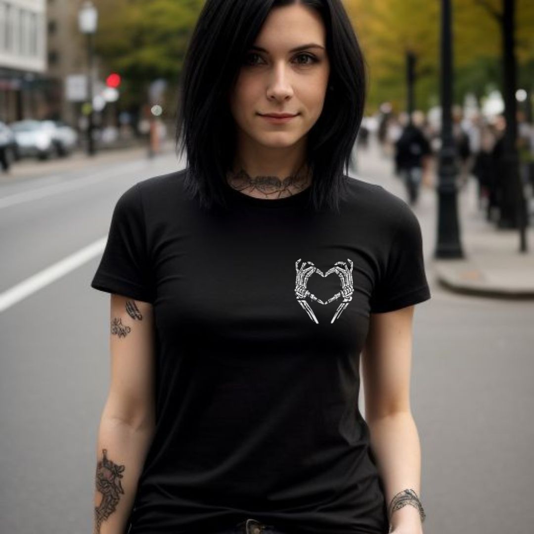 Woman standing in city with black hair and tattoos wearing a black slogan shirt that says I am who I am your approval is not needed with skull hands in the shape of a heart created by apparel company Midnight Gypsy Designs.