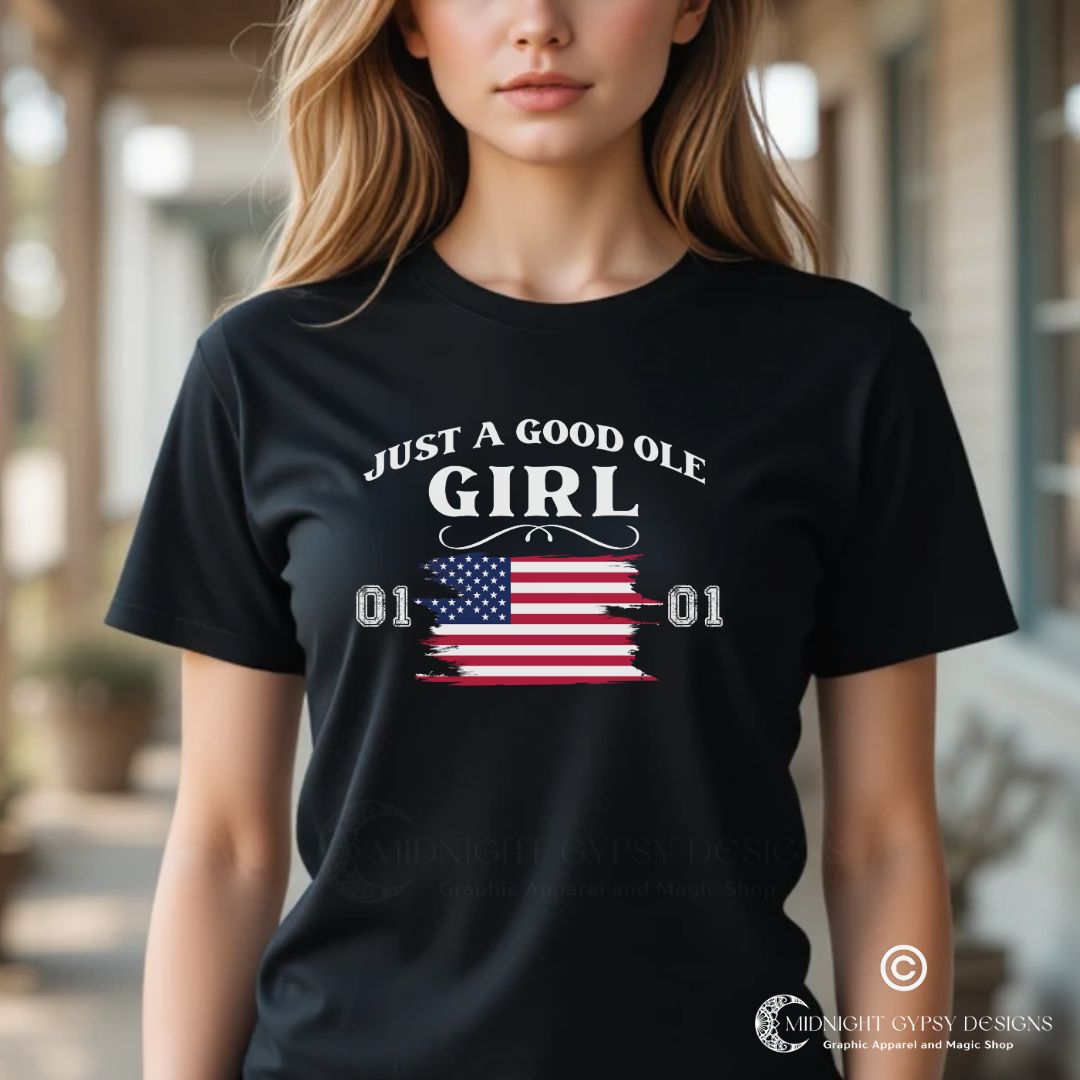 Young woman with long blonde hair standing outside on a southern porch wearing a black Just A Good Ole Girl shirt with American flag  and General Lee 01 number created by fandom graphic apparel company Midnight Gypsy Designs as part of their Patriotic Pride Apparel Collection. Perfect Dukes of Hazard shirt, Dukes of Hazard t-shirt, Daisy Duke shirt, Daisy Duke t-shirt, General Lee shirt, General Lee t-shirt, and  USA Patriotic shirt.