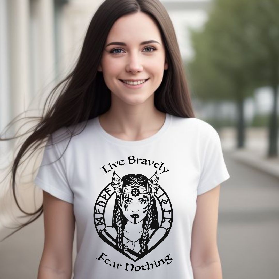 Young woman with long brown hair smiling while standing outside wearing a white t-shirt that reads Live Bravely Fear Nothing with a shield maiden Viking Warrior woman with Futhark runes created by apparel shop Midnight Gypsy Designs.