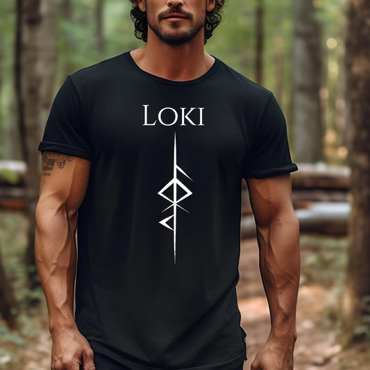 Man with dark near shaven beard and mustache with muscles standing in woods wearing a black t-shirt that reads Loki with the Loki Futhark rune symbol created by Norse Viking apparel shop Midnight Gypsy Designs. 