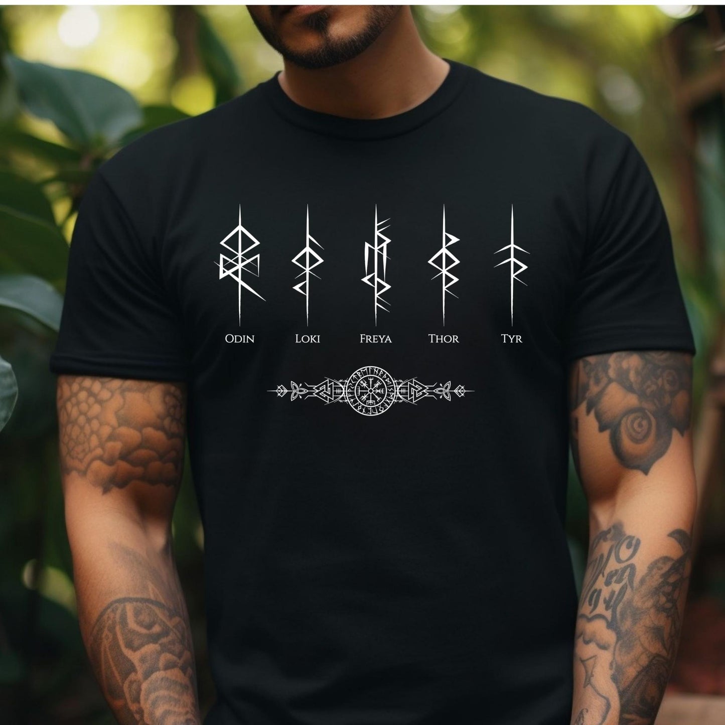 Young man with tattoos and muscles wearing a black t-shirt that reads Odin, Loki, Freya, Thor, and Tyr with Futhark rune symbols and vegvisir viking compass created by Norse Viking apparel shop Midnight Gypsy Designs. 