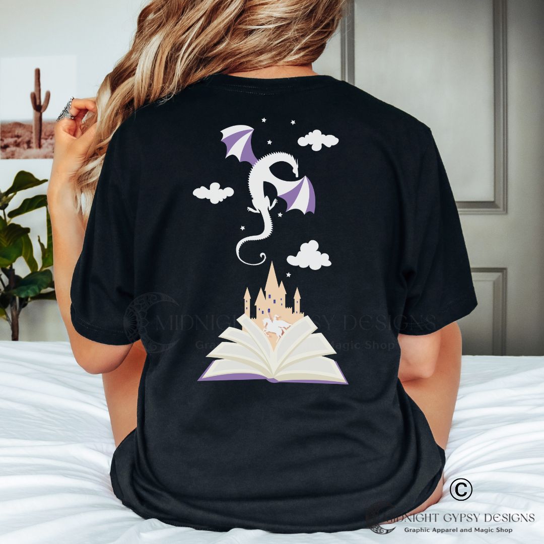 Woman with long blonde hair wearing a black reading is magic shirt with a dragon flying in clouds and stars over a castle and open book created by graphic apparel company Midnight Gypsy Designs as part of their bookish merch apparel line.