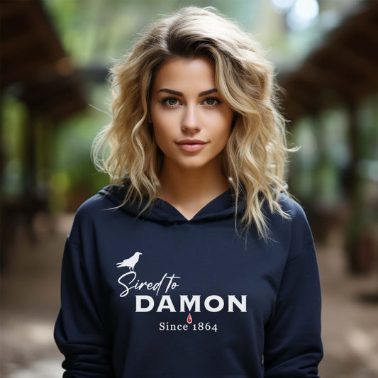 Young woman with wavy blonde hair wearing a Gildan navy The Vampire Diaries Sired to Damon Since 1864 hoodie with a crow and blood drip created by bookish shop Midnight Gypsy Designs.