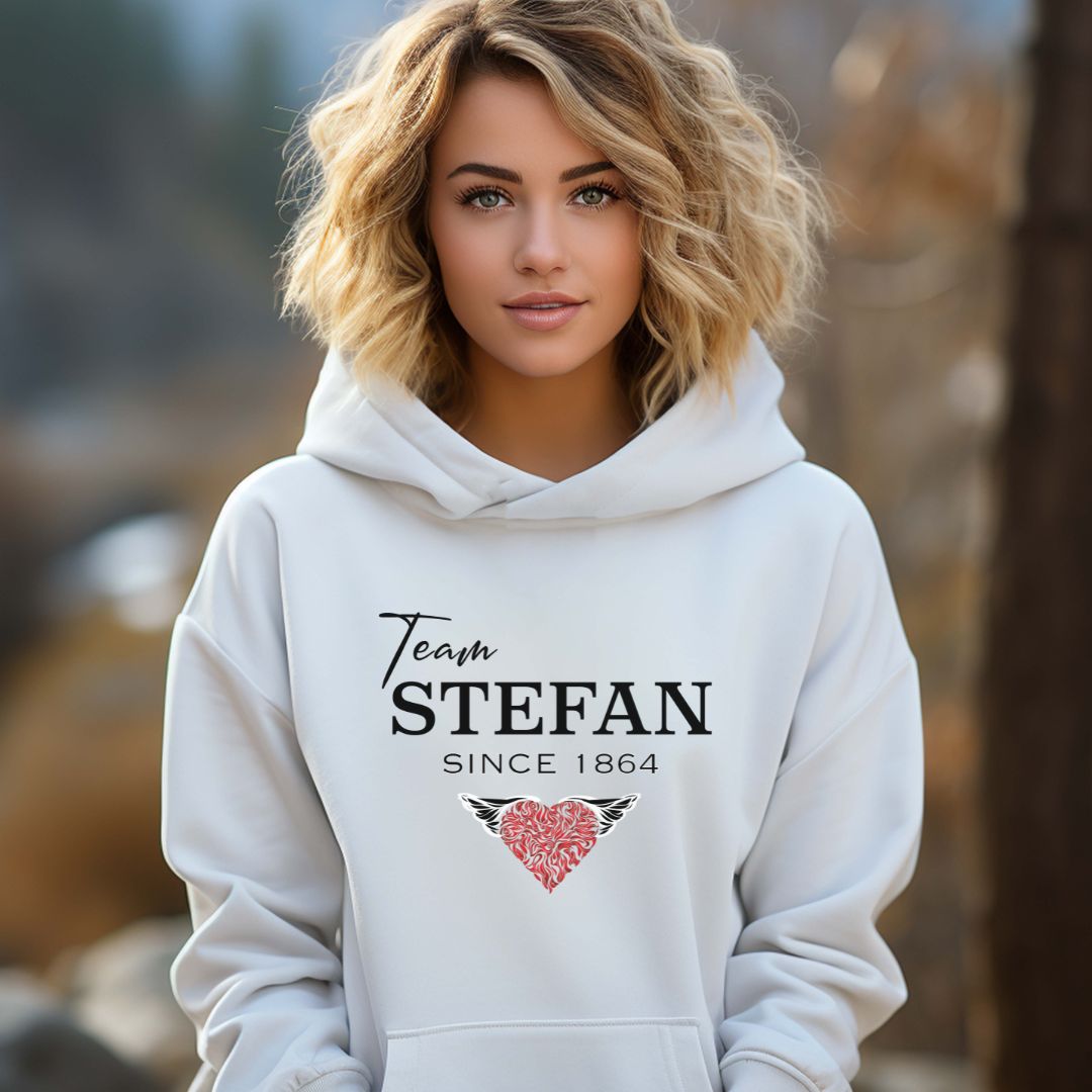 Young beautiful woman with curled blonde hair standing outside while wearing a Gildan white hoodie from The Vampire Diaries that reads team Stefan since 1864 with a read heart created by clothing apparel shop Midnight Gypsy Designs.