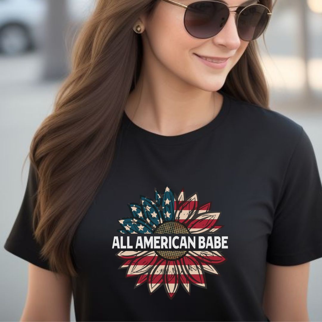 Woman with long brown hair wearing sunglasses and a black All American Babe patriotic t-shirt with an American flag sunflower created by USA patriotic apparel shop Midnight Gypsy Designs. 