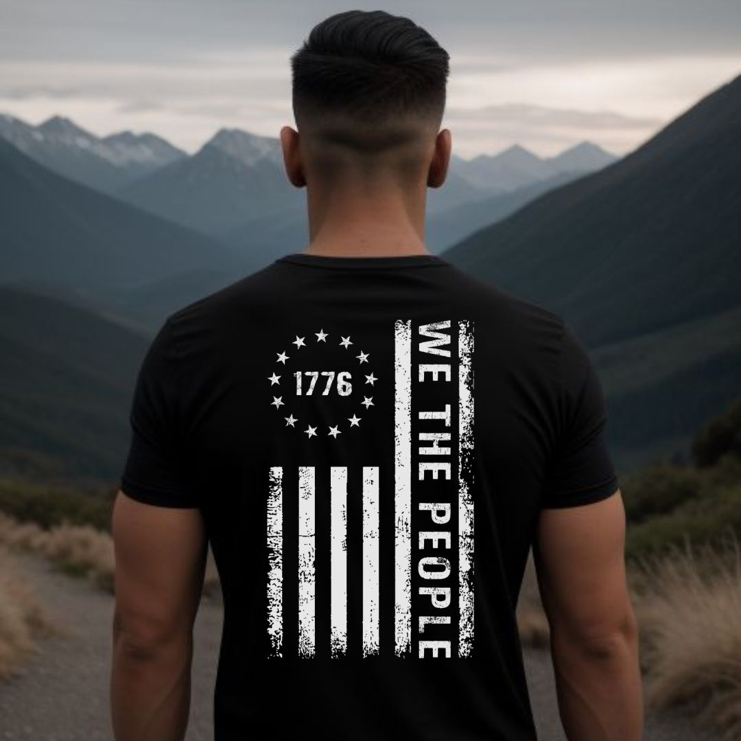 Man facing mountains with short hair wearing a black and white USA patriotic 1776 we the people t-shirt with USA flag and 13 colonial stars created by American patriotic clothing apparel shop Midnight Gypsy Designs.