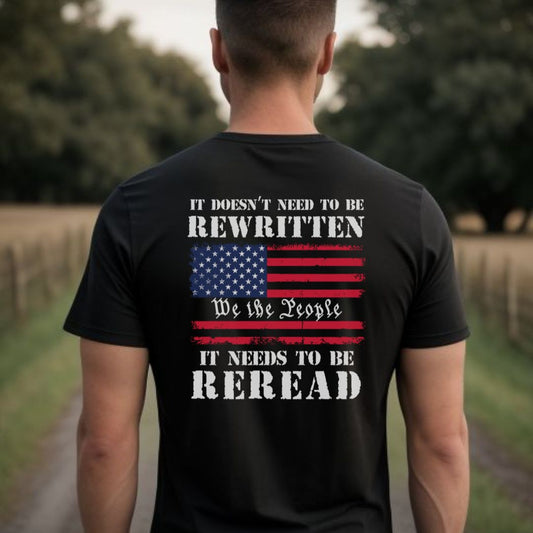 Young American man standing in field with black US Constitution patriotic t-shirt that says It Doesn't Need to be Rewritten it needs to be Reread with an American flag and We the People created by patriotic apparel shop Midnight Gypsy Designs