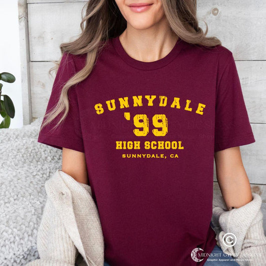 Young woman with blonde hair wearing a Buffy the Vampire Slayer Sunnydale High shirt in maroon with gold lettering created by graphic apparel company Midnight Gypsy Designs as part of their Buffy the Vampire Slayer merch line.