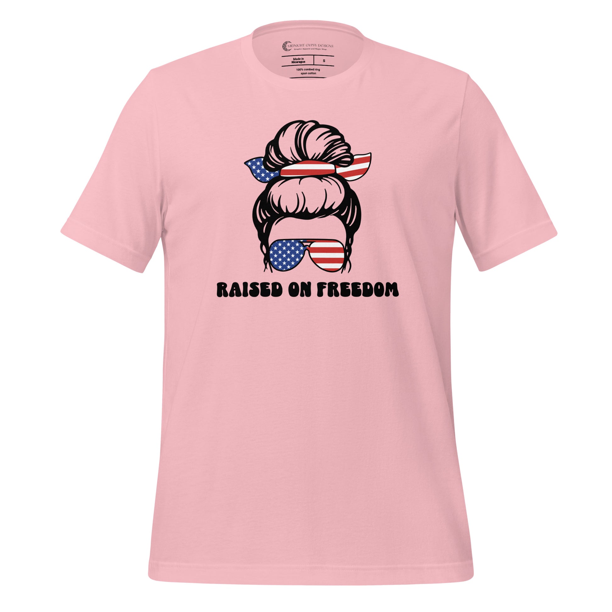 Pink Raised on Freedom shirt with graphic of a woman with an American flag hair tie and sunglasses created by graphic apparel company Midnight Gypsy Designs as part of their patriotic apparel collection. Perfect USA patriotic shirt, All American Girl shirt, girl power shirt, American pride shirt, USA shirt, USA flag shirt, womens patriotic shirt, Fourth of July shirt, Patriotic pride shirt, American flag shirt, Independence Day shirt, & American girl shirt.